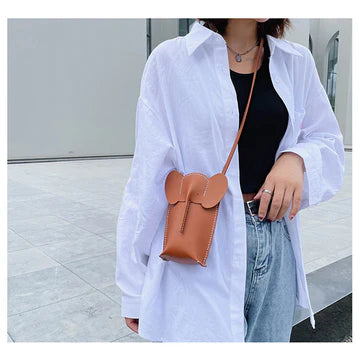 Person wearing a white shirt and blue jeans with a brown leather bag.